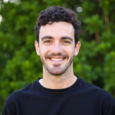 Nathan Grzesiek — a friendly portrait in a black shirt against a green, sunlit background.
